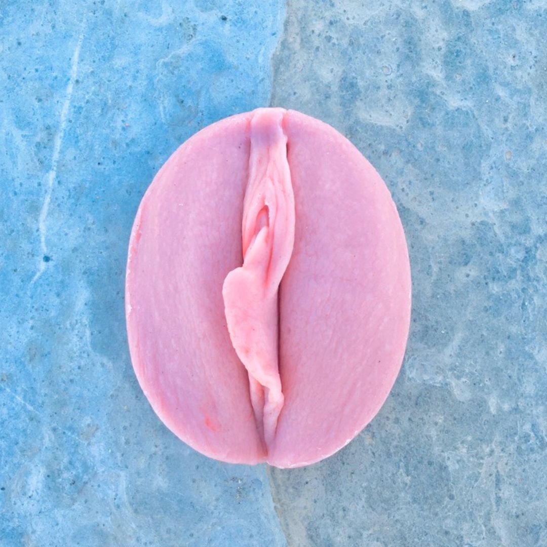 rosa Vulvaseife auf Stein, der wie Wellen im Wasser schimmert.